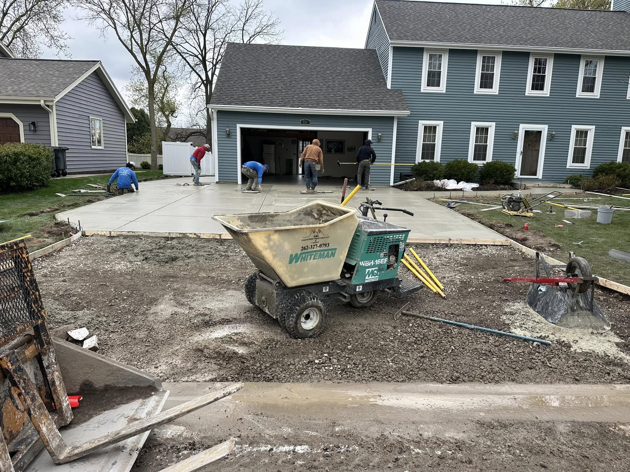 Crew screeding and finishing freshly poured concrete driveway with power buggy and wheelbarrow in foreground